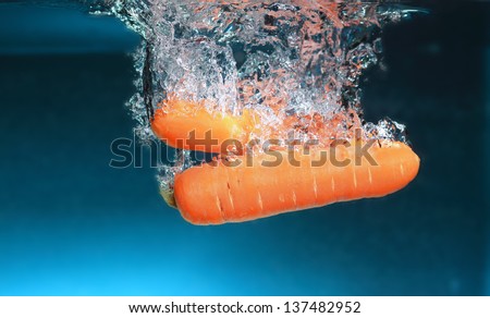 Carrot in the water splash over blue background. Healthy food and active life.