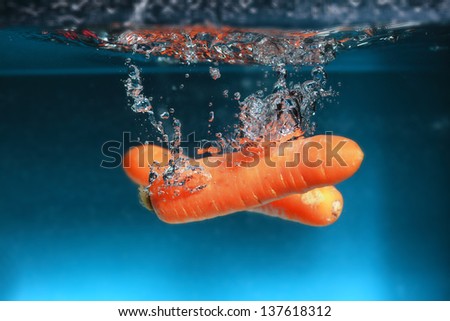 Carrot in the water splash over blue background. Healthy food and active life.