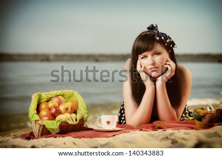 Picnic outdoors. Beautiful woman lying on red blanket on sandy beach. Retro style.