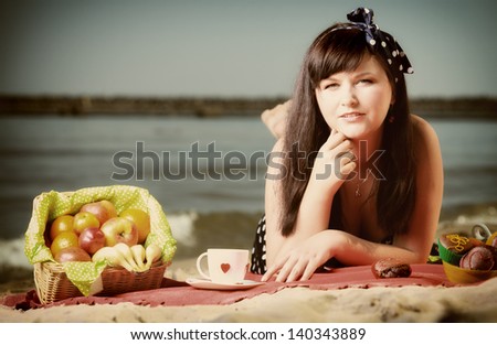 Picnic outdoors. Beautiful woman lying on red blanket on sandy beach. Retro style.
