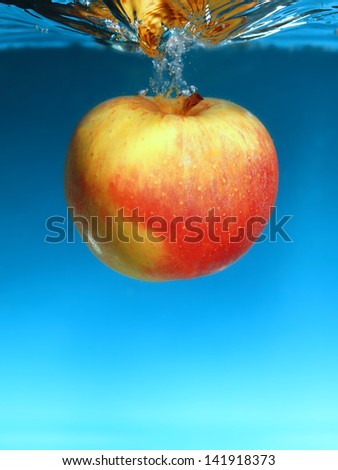 Yellow red apple in the water splash over blue background. Healthy food and active life. Square format.