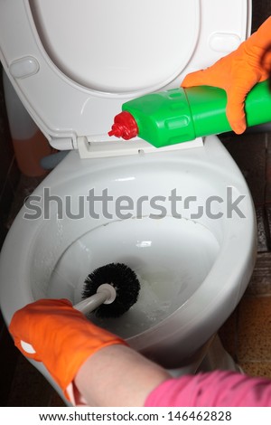 Female hand in orange rubber glove cleaning toilet bowl using brush. Clean up your house.