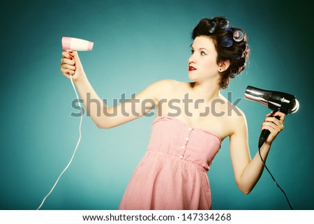young woman preparing to party having fun, funny girl styling hair with curlers and hairdreyer retro style blue background