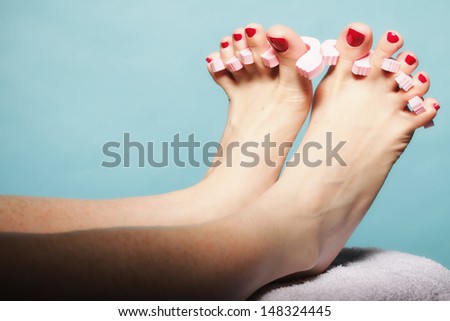foot pedicure applying woman\'s feet with red toenails in pink toe separators blue background