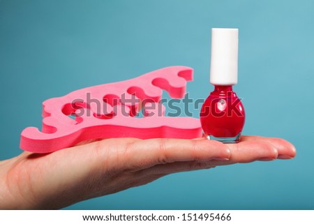 Pedicure accessories red nail polish and pink toe separators on female hand blue background