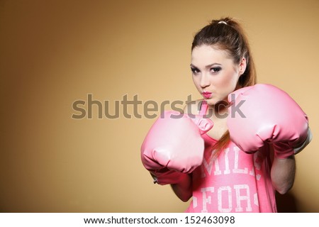 Female boxer model wearing big fun pink gloves playing sports boxing studio shot, brown background