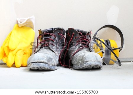 Renovation at home. Construction equipment tools work boots yellow protective noise muffs gloves in building site.