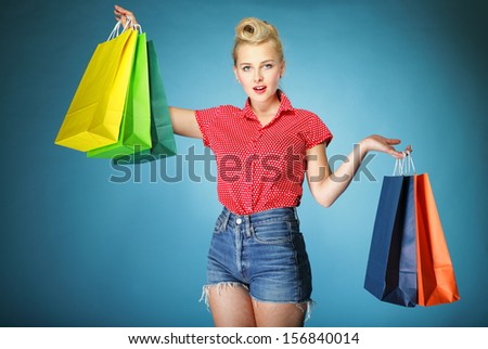 Retro style. Young woman in red dotted shirt and shorts with colorful shopping bags isolated on blue background