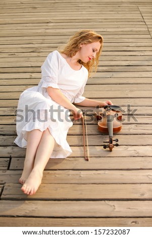 The blonde girl music lover on pier with a violin. Love of music concept.