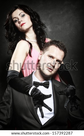 Retro style attractive fashionable couple in love, rich gangster with charming woman on black background