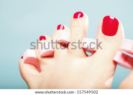 foot pedicure applying woman\'s feet with red toenails in pink toe separators blue background