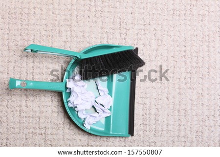 Green sweeping brush and dustpan for house work with garbage papers on floor indoors. Cleaning