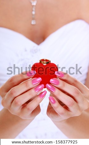 Female hands of bride in white dress with engagement or wedding ring in red heart shaped box. Close up.