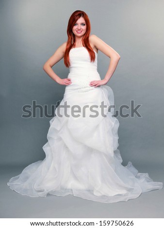 Wedding day. Portrait of happy beautiful blue eyed red haired bride long white dress in full length studio shot on gray background