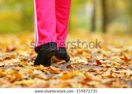 Runner legs and running shoes. Sporty woman jogging walking outdoors in autumn park on forest path, fall colors golden leaves