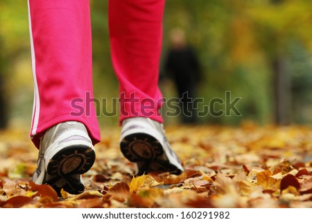 Runner legs and running shoes. Sporty woman jogging walking outdoors in autumn park on forest path, fall colors golden leaves