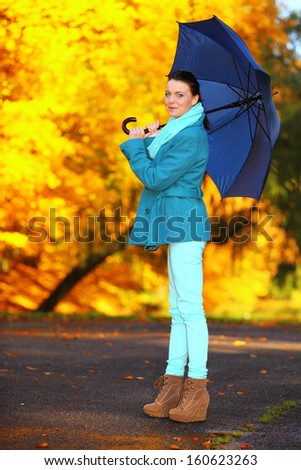 Fall lifestyle concept. Casual young woman girl walking with blue umbrella in autumnal park. Yellow gold colorful leaves background