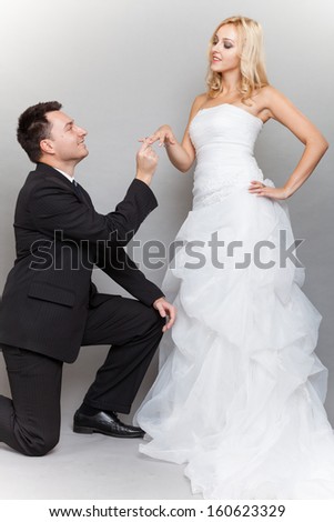 Wedding day. Groom putting a wedding ring on bride\'s finger studio shot gray background