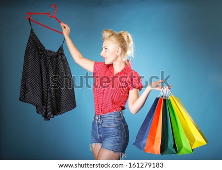 Retro style. Shopper woman happy shopping buying clothes. Pinup girl holding colourful shopping bags in one and rack with clothes in another hand on blue background