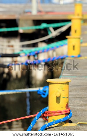 harbor quayside old yellow mooring bollard with blue red rope in marina