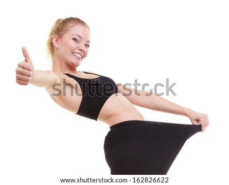Weight loss, healthy lifestyle. Blonde happy excited woman fitness girl with big pants, showing how much weight she lost, giving thumbs up success hand sign isolated on white background