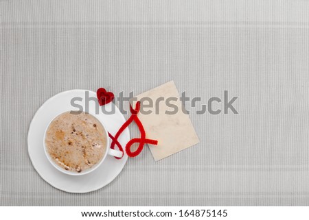 White cup of hot beverage drink coffee cappuccino latte with heart shape symbol love and blank paper card space for text message. Valentine\'s day.