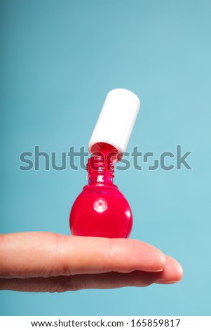 Pedicure manicure red nail polish bottle on female hand blue background