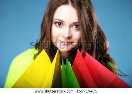 young woman in bright vivid colour sweater with paper multi coloured shopping bags on blue background. Sales and discounts concept.