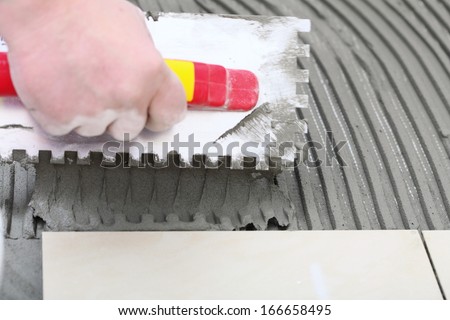 Home improvement, renovation - construction worker tiler is tiling, ceramic tile floor adhesive,  trowel with mortar