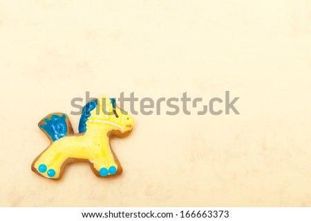 Homemade gingerbread cake pony with icing and blue yellow decoration on brown paper background. Christmas and holiday handmade concept.