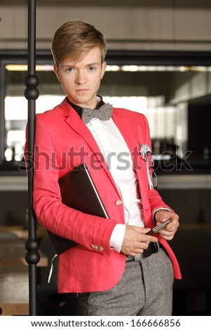 Young handsome stylish man fashion model wearing bright red jacket and bow tie with notebook posing indoor