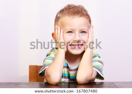 Portrait of surprised excited emotional blond boy child kid at the table interior. Emotions.