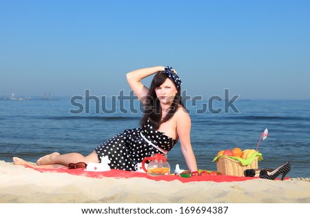 Picnic outdoors. Beautiful woman sitting on red blanket on sandy beach. Retro style.