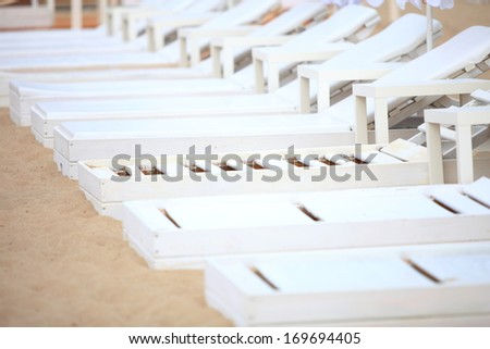 Row of empty white pool plastic chairs deckchairs on sand beach. Vacation concept