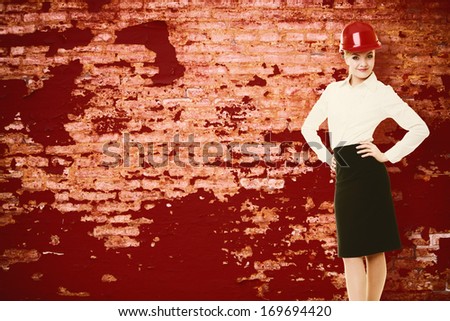 Portrait of attractive female engineer. Woman architect in red safety helmet on old grunge brick wall background with blank copy space. Building.