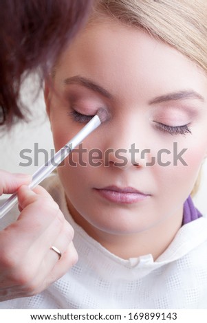 Make-up artist applying with brush color eyeshadow on female eye holding shell with eye-shadows, close up