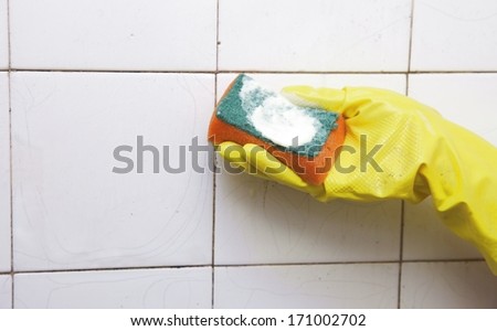 gloved hand cleaning dirty old tiles with sponge in a bathroom
