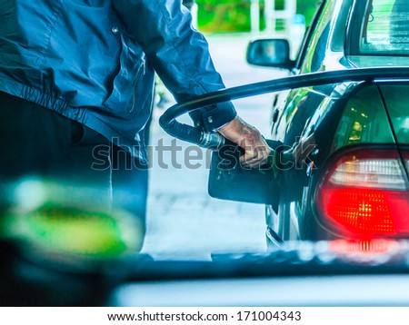 Male hand refilling the car with gas or petrol on filling station, holding a fuel pump outdoor