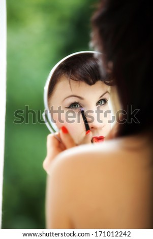 young woman preparing to party, girl applying make up looking at mirror retro style green blured background