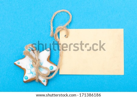 Homemade gingerbread cake star with icing and blue decoration and blank paper card copy-space on blue as christmas background. Holiday handmade concept.
