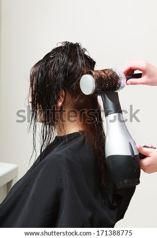 Hairstylist with brush and dryer. hairdresser drying hair of female client. Woman in hairdressing beauty salon.