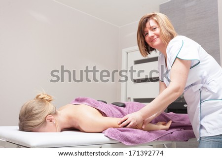 Day-spa. Therapist in work and female customer. Young woman relaxing in healthy spa salon. Girl having hot stone massage. Indoor.