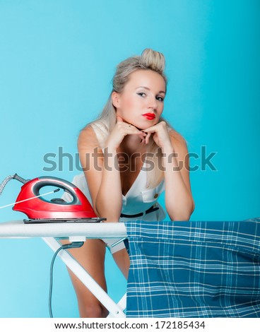 Sexy girl retro style ironing male shirt, woman housewife in domestic role. Traditional sharing household chores.  Pin up housework.  Vivid blue background