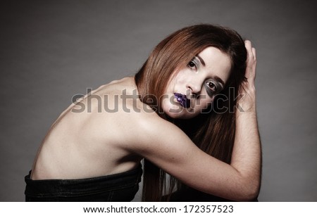Sad young woman with long hair and creative makeup. Unhappy girl in gothic style on dark background. Negative emotions. Studio shot.