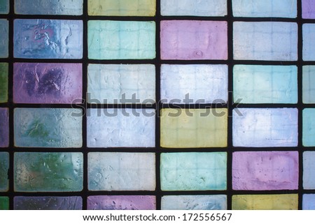 multicolored stained glass window with regular block pattern in hue of blue green violet