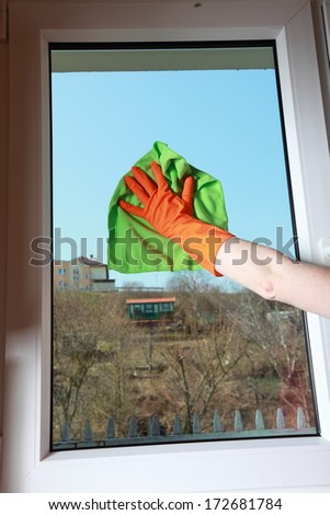 hand in orange glove cleaning window with green rag