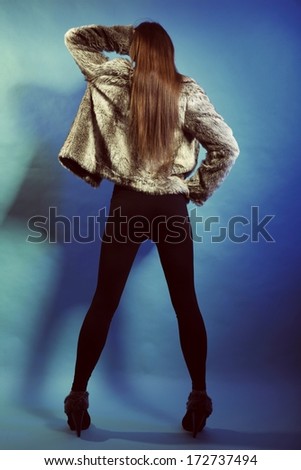 Full length fashionable woman in fur coat long hair back view blue background