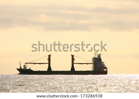 Transportation, cargo conteiner ship sailing in still water heading for the port against sunset sky