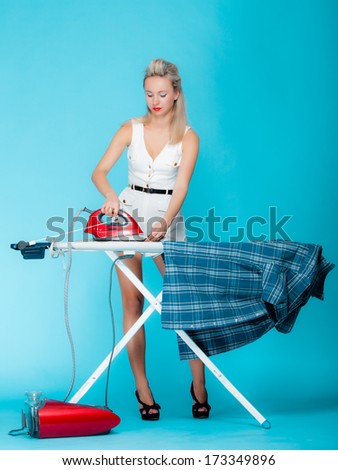 Full length sexy girl retro style ironing male shirt, woman housewife in domestic role. Traditional sharing household chores.  Pin up housework.  Vivid blue background