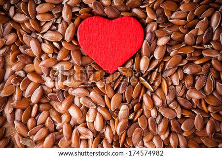 diet healthcare concept. Brown raw flax seeds linseed as natural background and red heart symbol. Healthy food  for preventing heart diseases. Flaxseeds are full of omega-3 fatty acids.
